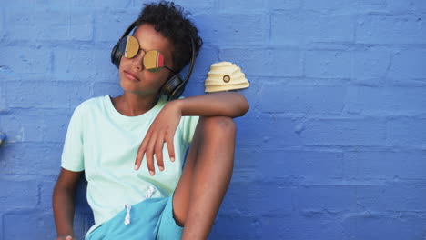 a young african american student relaxes against a blue background with copy space