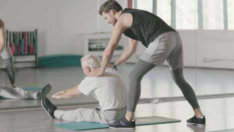 entrenador deportivo ayudando a un hombre jubilado a hacer ejercicios de estiramiento en el club de fitness.