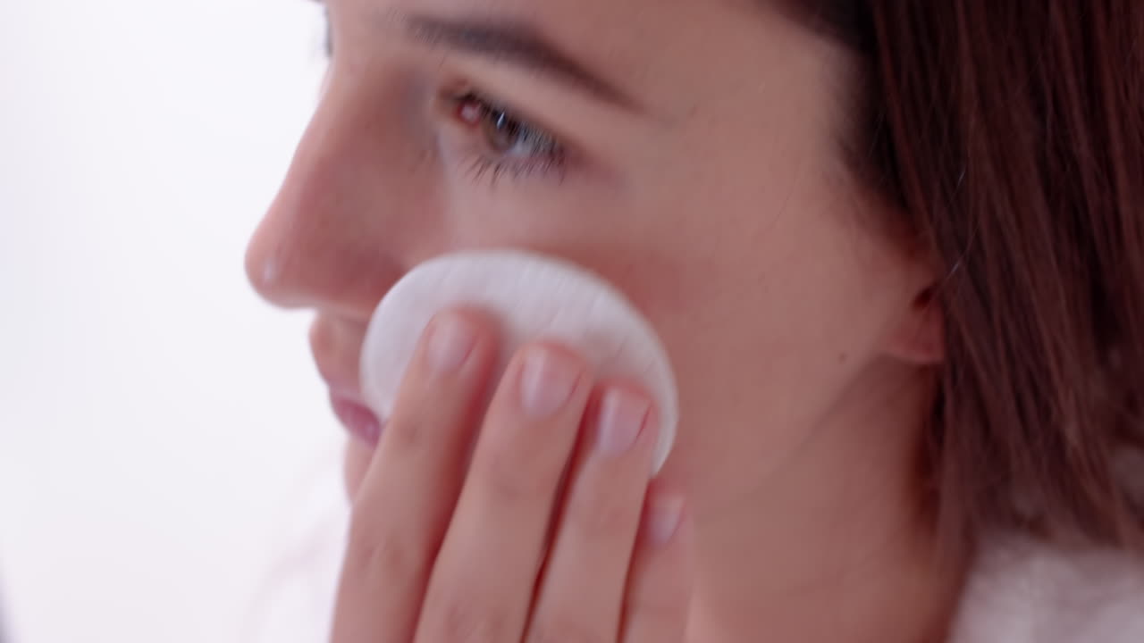 Using cotton pad, woman cleansing face for skincare routine at home spa