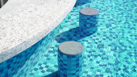 slow motion shot of concrete seats at the side of a pool bar with water reflecting