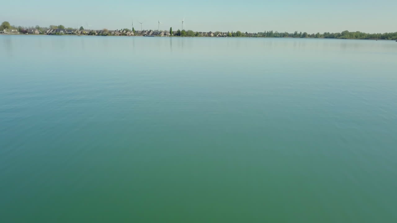Aerial drone shot of flying low at the lake and moving forward revealing the suburban near the lake in the Netherlands.