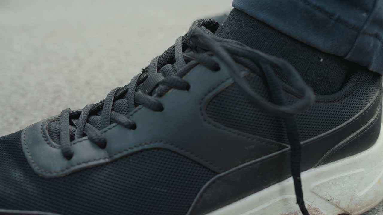 Allaccio individuale di lacci sul marciapiede urbano, uomo che allaccia le scarpe da ginnastica sulla strada cittadina durante le ore mattutine, impiegato che allaccia con cura i lacci scuri delle scarpe sul marciapiede prima di andare al lavoro