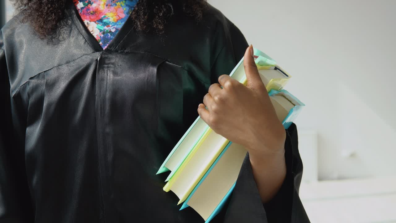 varios libros de texto en posición vertical en la mano de una estudiante afroamericana con una túnica negra. vista de libros y manos de cerca sobre un fondo blanco.