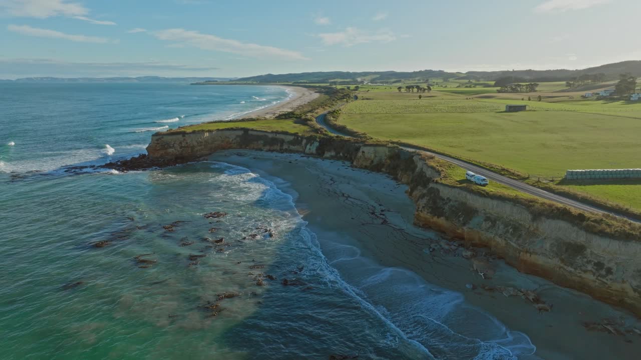 Stunning rotating aerial of tourist campervans parked in beautiful coastal location and overlooking Mitchells Rocks with sea views in Otago, South Island of New Zealand Aotearoa