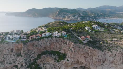 Aerial-approach-toward-rugged-seaside-cliff-with-buildings,-Mallorca