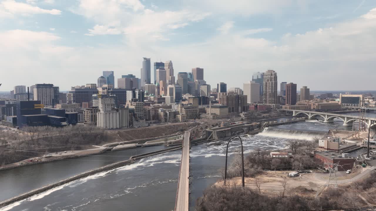 Timelapse aerial of Minneapolis skyline with St. Anthony Falls and Stone Arch Bridge with rays of light shinning through clouds.