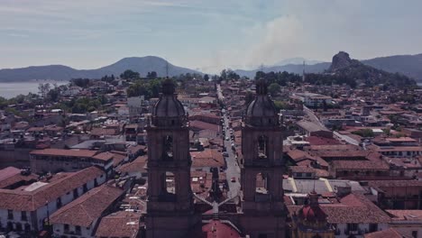 Toma-Trasera-De-Un-Dron-Pasando-Entre-Las-Torres-De-La-Parroquia-De-San-Francisco-De-Asís-En-El-Centro-De-Valle-De-Bravo-En-Un-Día-Soleado.