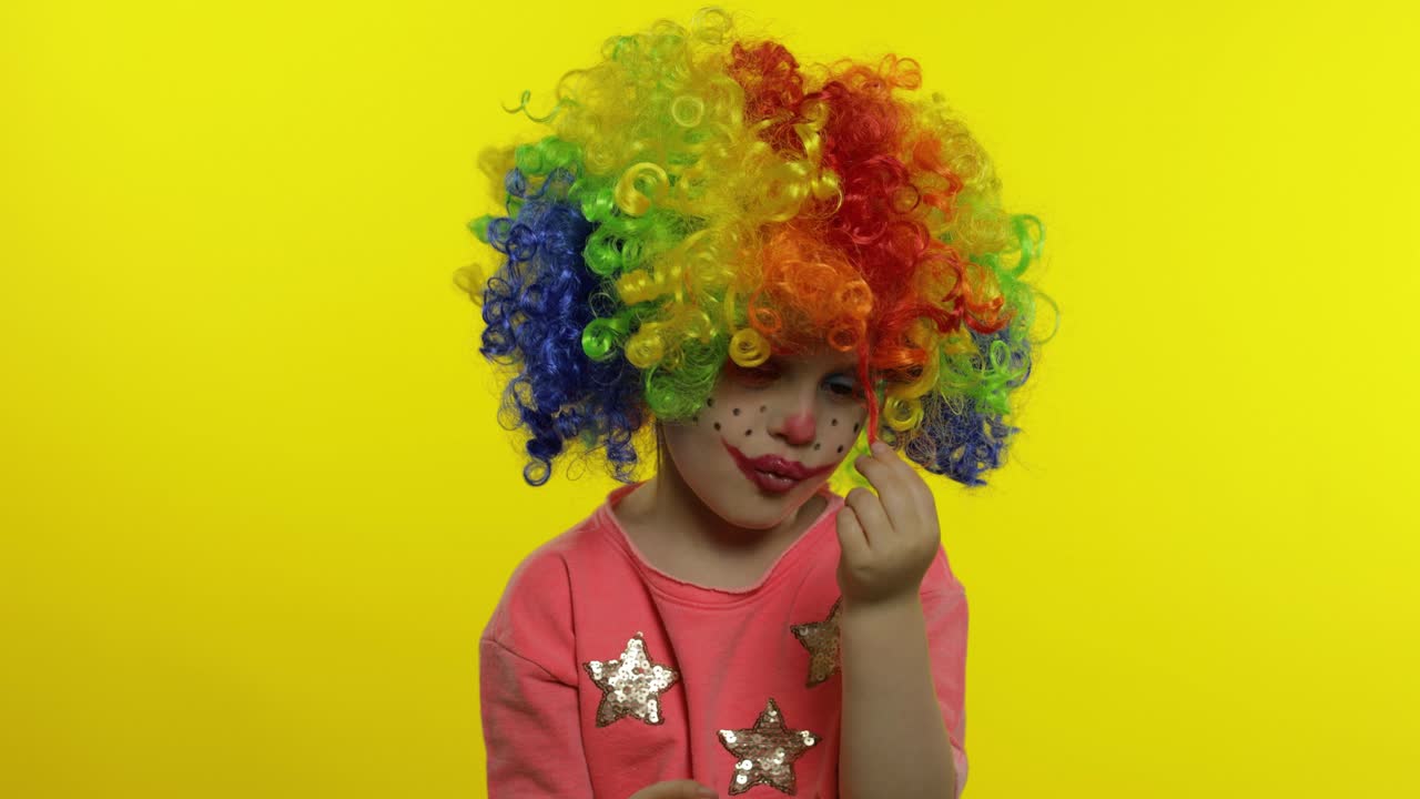 una niña payasa con una peluca arco iris haciendo caras tontas. tonto, sonriendo, bailando. halloween