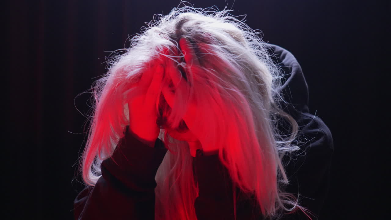 빨간 불이 켜진 방에서 긴장한 채 머리를 잡고 있는 금발 여성