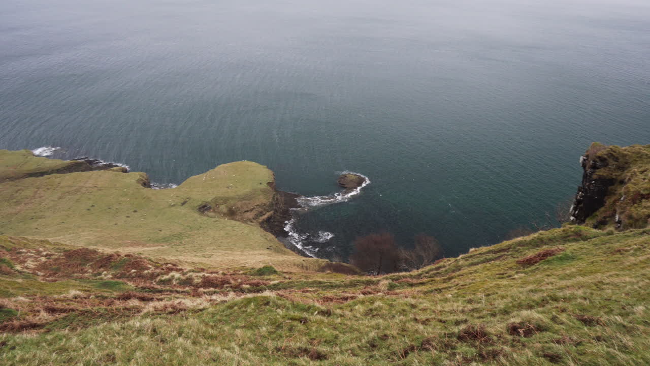 toma panorámica desde el borde de un acantilado de olas del océano atlántico salpicando la costa en un día lluvioso y nublado en escocia, isla de skye