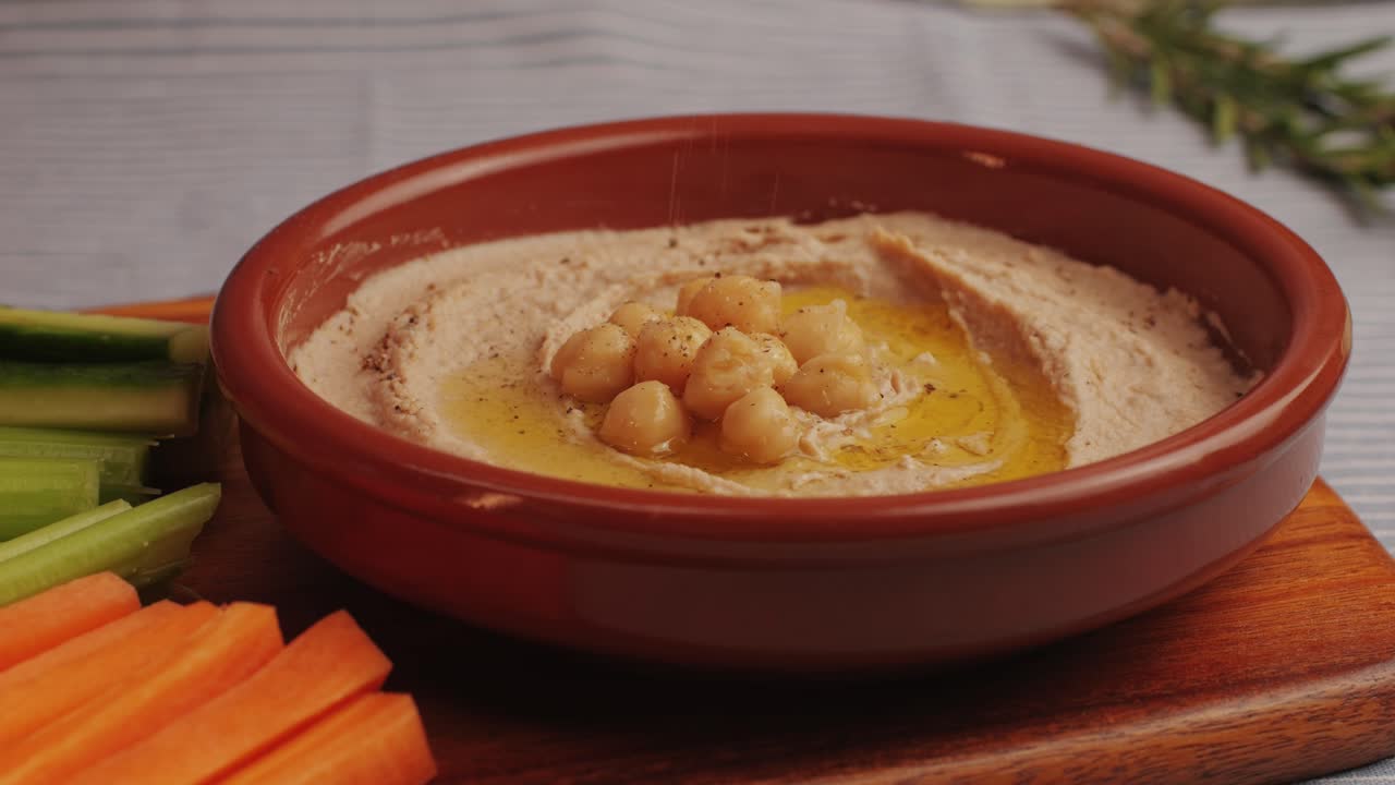 Hummus among fresh vegetables on table close-up. Pouring vegetables slice in hummus. Hummus or fava, a healthy snack of legumes and chickpeas. Kosher healthy vegan food. Lean, vegetarian dish. High quality 4k footage
