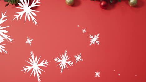 Animation-of-snow-falling-over-christmas-baubles-on-red-background