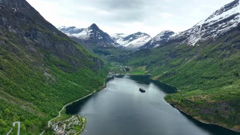 stunning geiranger fjord with mountain scenery in background - forward moving aerial from eagles road looking towards geiranger village with a cruise ship at anchorage