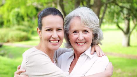 mother and adult daughter hugging and smiling at camera in the park