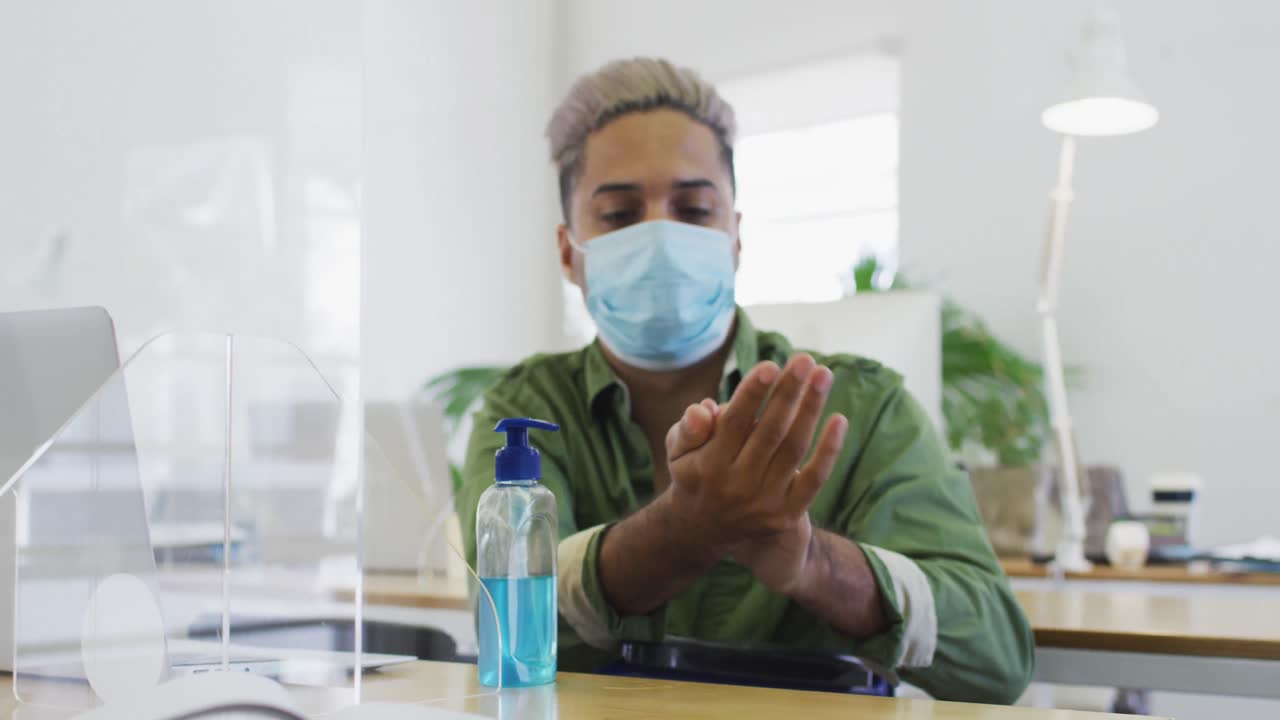 hombre con máscara facial desinfectando sus manos en la oficina