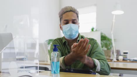 Man-wearing-face-mask-sanitizing-his-hands-at-office