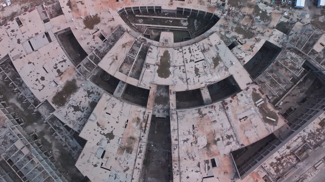 Overhead drone of a derelict circular complex concentric concrete slabs, cracked surfaces, exposed structure, debris-filled voids gritty demolition urbex visual for disaster or redevelopment themes