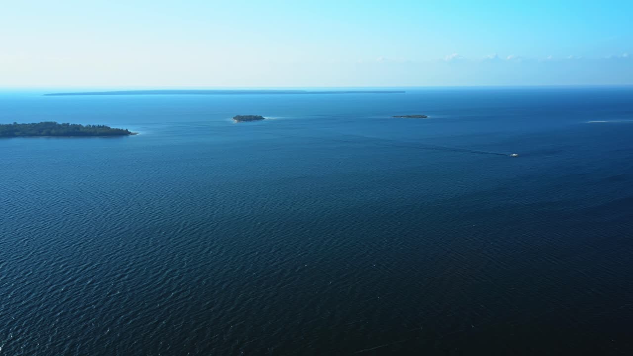 Tiny islands drift within the endless blue of Lake Michigan, their green canopies punctuating the calm expanse of water that stretches toward the hazy horizon of Door County