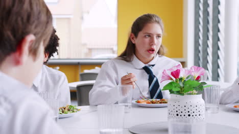 grupo de estudiantes de secundaria vestidos de uniforme sentados alrededor de la mesa y comiendo almuerzo en la cafetería