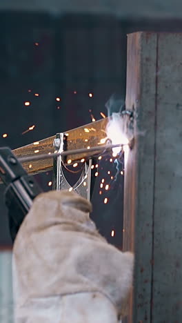 slow motion closeup builder in work gloves welds plank to fence pole with sparks at country house