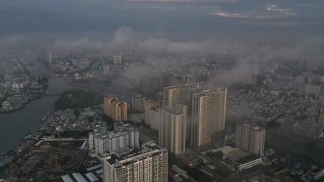 Early-morning-urban-drone-shot-flying-in-over-high-rise-apartment-buildings-and-canal-in-populated-area-of-Ho-Chi-Minh-City-with-heavy-fog-and-low-clouds