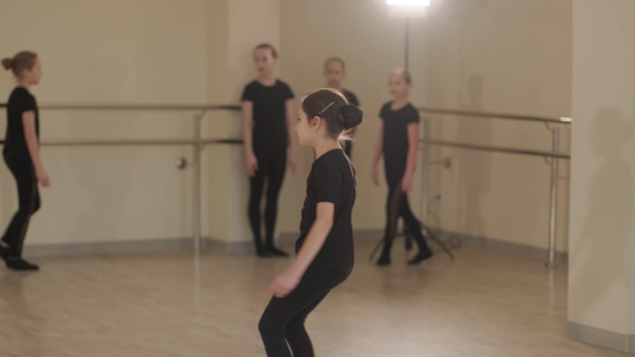 un grupo de jóvenes estudiantes de ballet con ropa de baile negra practicando posiciones en un amplio estudio de ballet con pisos de madera y barras montadas en la pared. expresiones enfocadas y movimientos sincronizados.