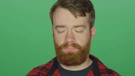 young bearded man looking sad, on a green screen studio background
