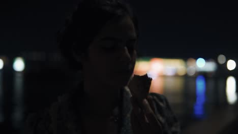 A-young-Indian-girl-eats-a-frozen-cone-at-night-in-the-city-on-the-river-bank