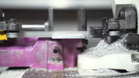 máquina de sierra automática cortando una placa de metal dejando aserrín metálico