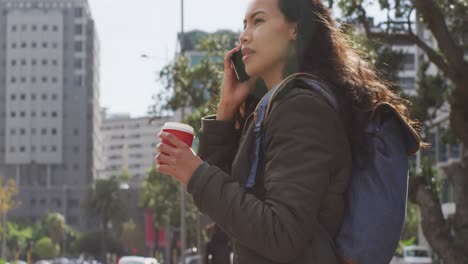 asian woman holding coffee cup talking on smartphone while standing on the street