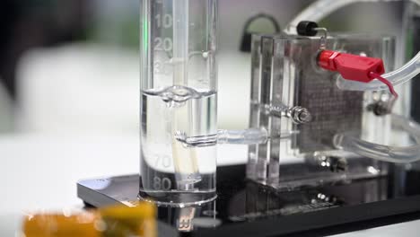 hydrogen bubbles forming in a plastic cylinder pressing the water out of the tube, a fuel cell demonstrator splits water into oxygen and hydrogen, slow motion, slow zoom in