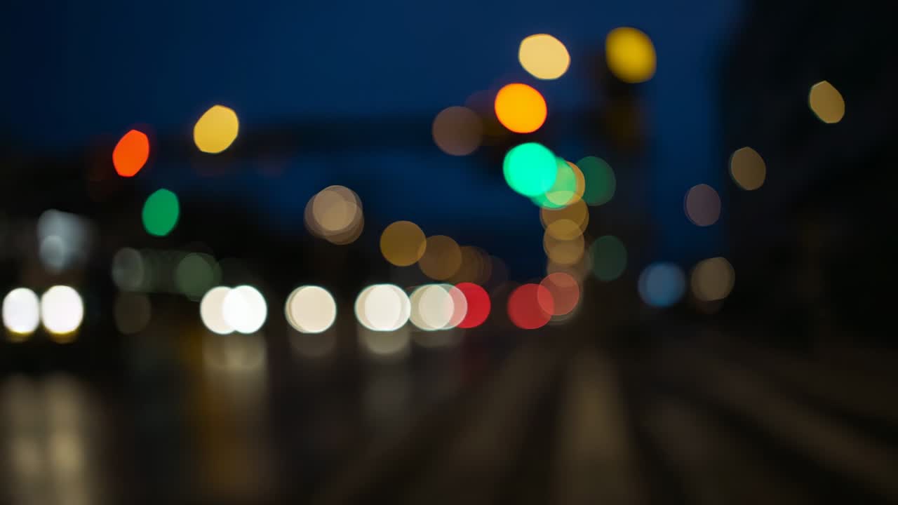 Stationary camera recording blurred headlights, taillights and signals shifting on wet night street