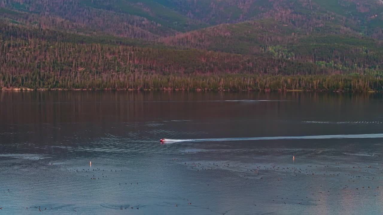 Drone orbit around boat racing across Grand Lake Colorado as twilight colors reflect on water