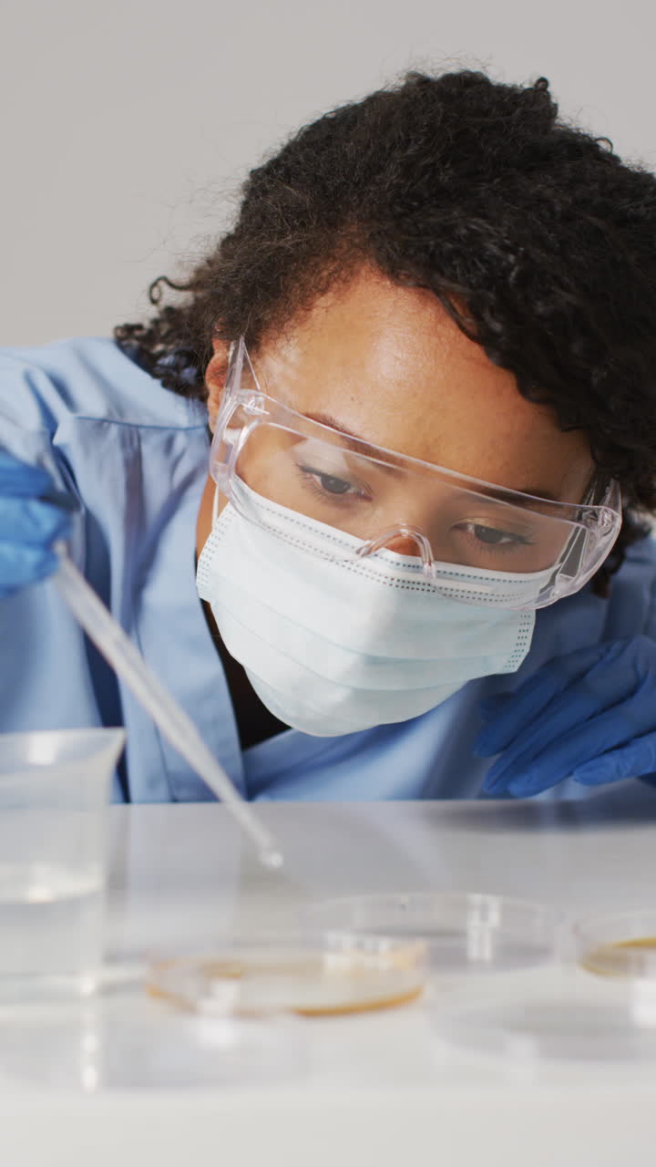 Vertical video of happy biracial female lab worker in face mask