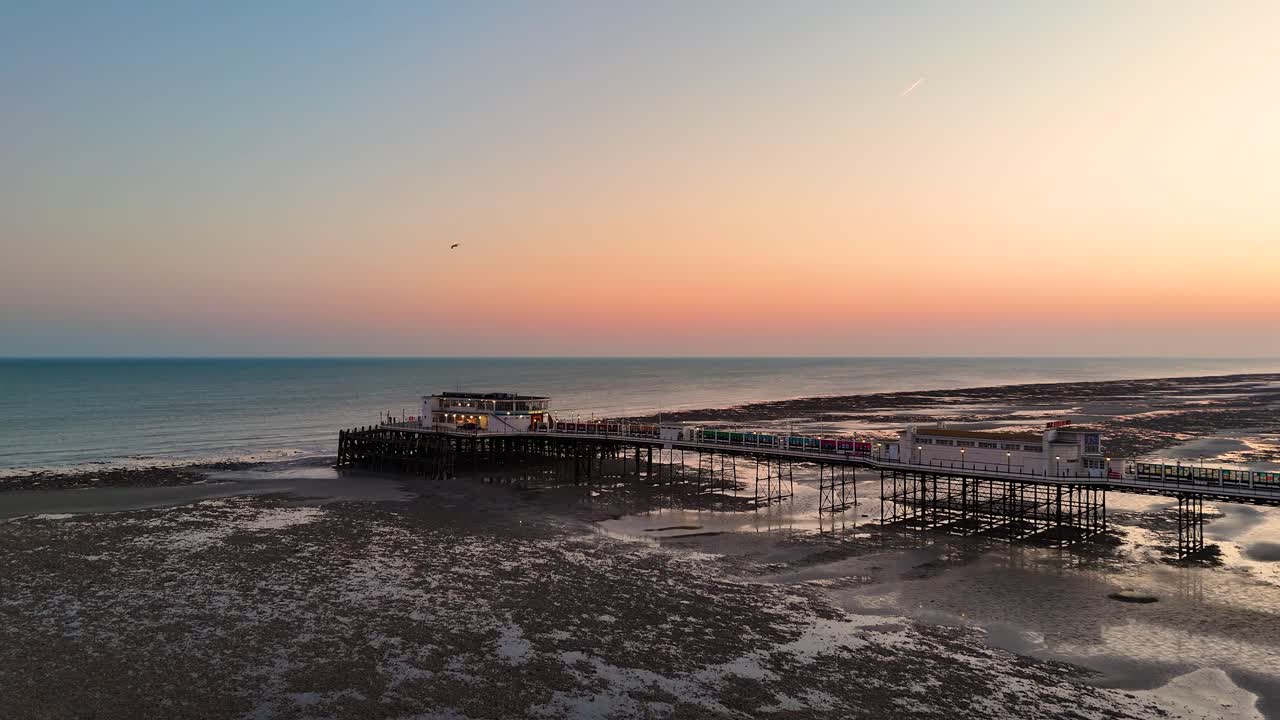 Cảnh quay drone từ trên không bến tàu Worthing Pier, Sussex, Vương quốc Anh khi thủy triều xuống vào một buổi tối xuân yên bình, để lộ kết cấu đáy biển, các mô hình ven biển và ánh sáng giờ vàng dịu nhẹ
