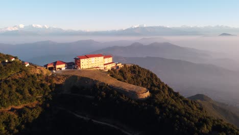 kathmandu, nepal - december 12, 2021: an aerial view of a resort perched on a hilltop with the himalayan mountain range in the background