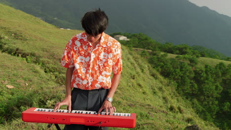 Asian-guy-playing-keyboard-at-mountain-in-Vietnam,-orbital-handheld-slow-motion