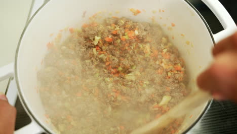 minced beef and vegetables are being cooked in a cast iron pot chef stirring while the ingredients are steaming and smoking