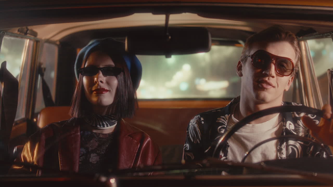 Pareja joven con atuendos elegantes disfrutando de la música durante un paseo nocturno en un coche retro.