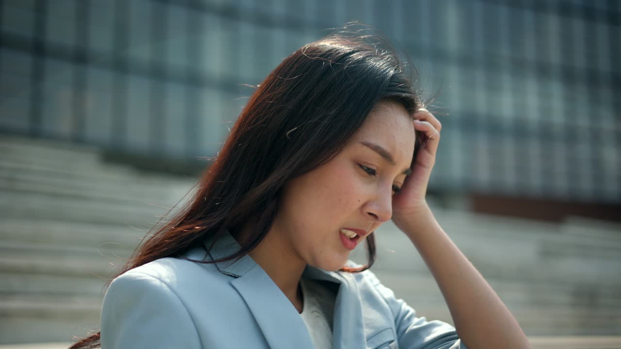 도심의 사무실 건물 근처의 계단에서 노트북에서 일하는 심각한 사업가 여성. 온라인 회의에 노트북을 사용하는 불행한 여성.