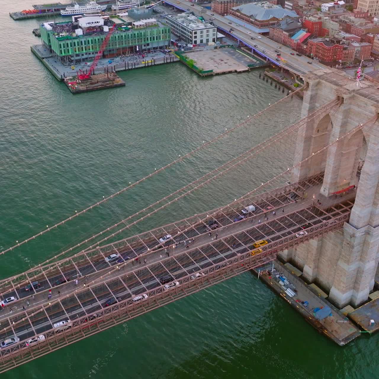Famous Brooklyn Bridge over East River in New York. Numerous cars going along the bridge and yacht coming under it. Aerial view