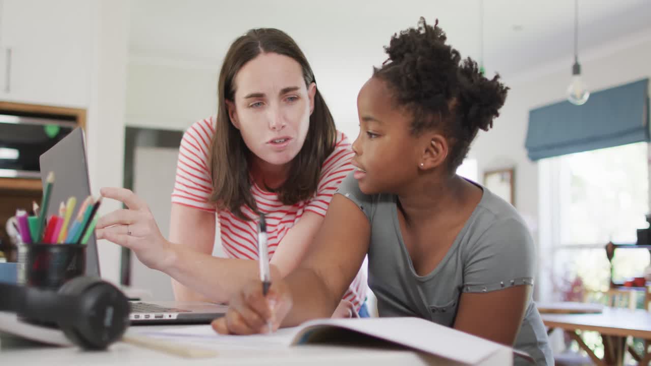Happy caucasian woman and her african american daughter doing homework together