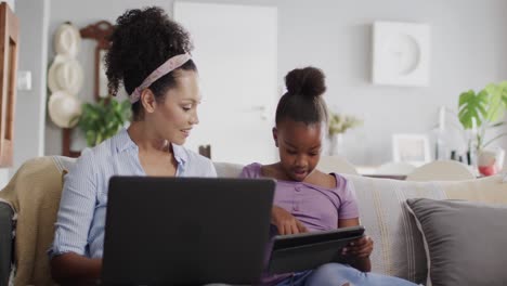 Glückliche-Afroamerikanische-Mutter-Und-Tochter-Sitzen-Auf-Dem-Sofa,-Benutzen-Laptop-Und-Tablet,-Zeitlupe