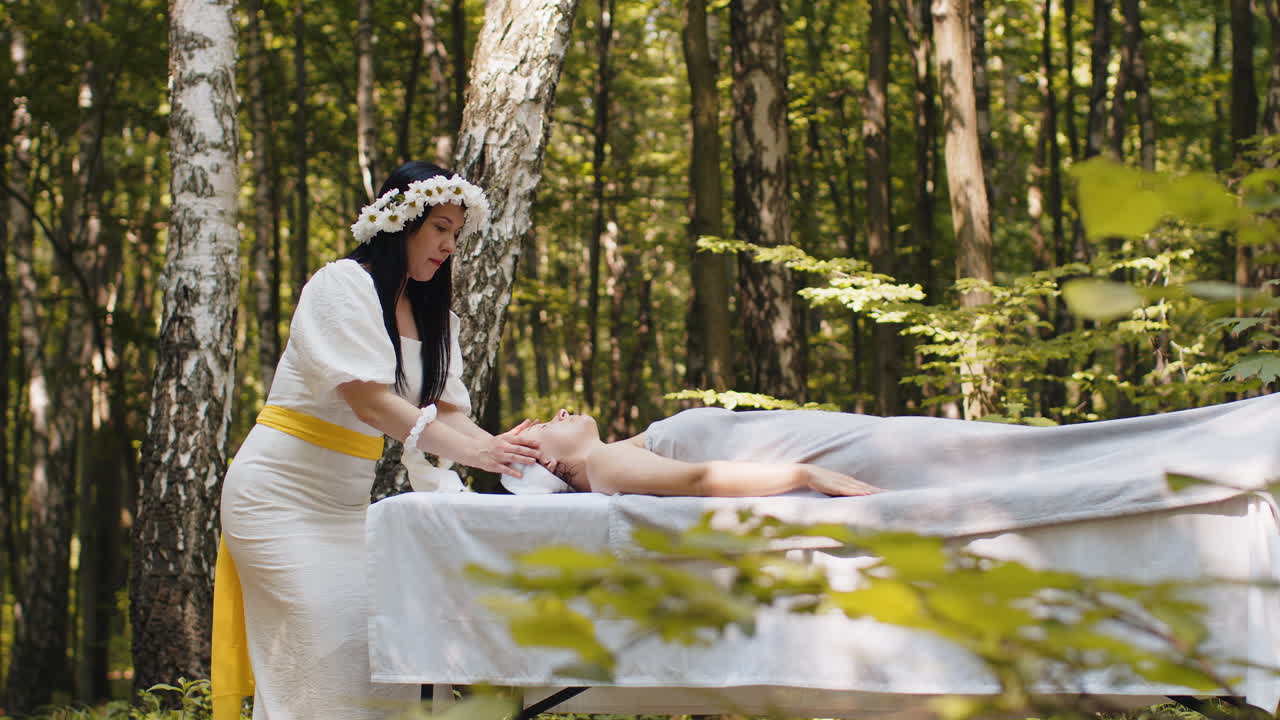 치료사 여성 의사는 숲에서 야외에서 손으로 스파 얼굴 마사지를하는 여성을 편안하게 만니다.