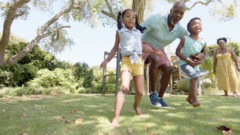 happy african american grandparents with grandchildren playing football in garden, in slow motion