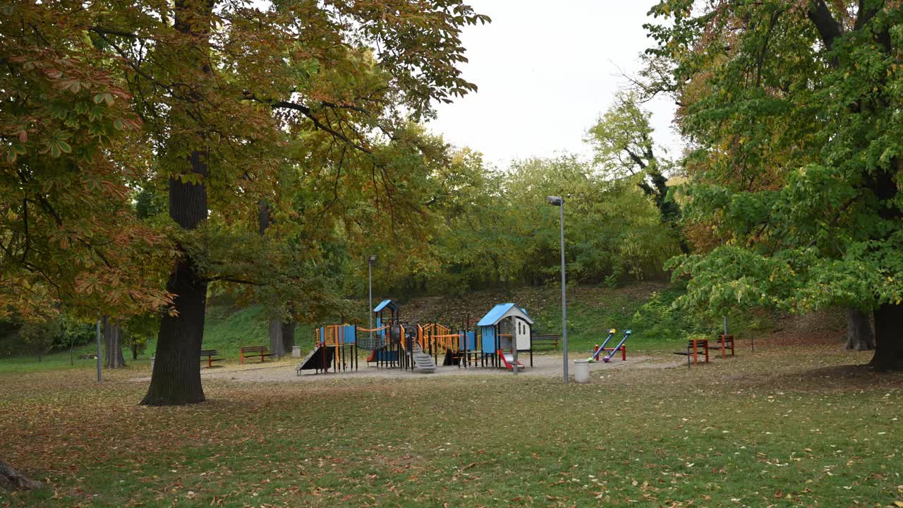 Empty children’s playground in public park on quiet autumn morning, fallen leaves covering the ground, 4K with selective focus