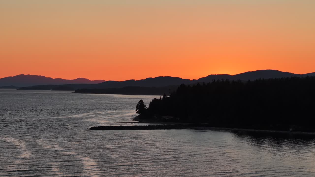 A sunset on the Sunshine Coast with a rocky point and layers of mountains in the distance. The ocean meets the deep oranges of the sky,