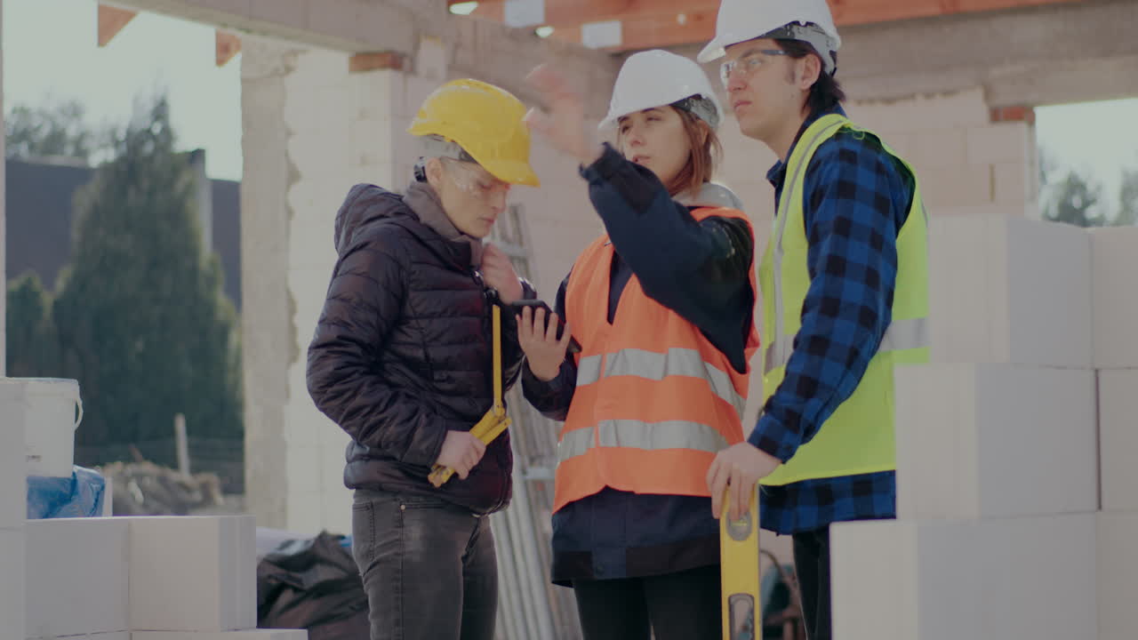 Young female and male coworkers discussing over smartphone with engineer at construction site