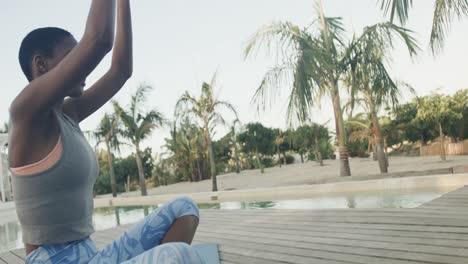 Relaxed-biracial-woman-practicing-yoga-meditation-sitting-on-jetty-at-beach,-copy-space,-slow-motion