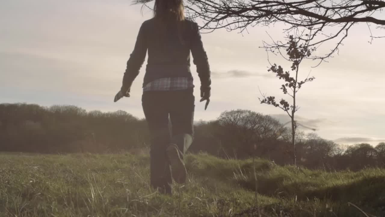 Woman walks in countryside field landscape with overhanging tree branch